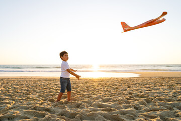 Child throws toy plane into air at the beach.