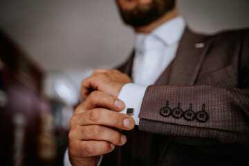 Valmiera, Latvia- July 28, 2024 - In close-up, a man secures a silver cufflink on his shirt's cuff,...