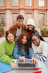 Vertical. Diverse group of cheerful teenage students is huddled together in the university campus, diligently working on a assignment using their laptop, focused on gathering information from computer