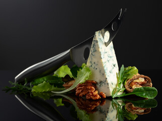 Blue cheese with knife, walnuts and fresh greens.