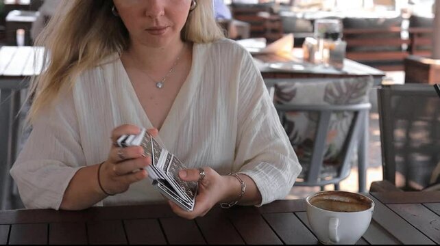 Woman in a light outfit reads Tarot cards on a table in a cafe