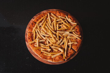 Overhead view of a French fries pizza on a black granite table.