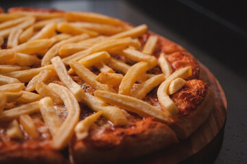 Detail view of a French fries pizza on a black granite table.