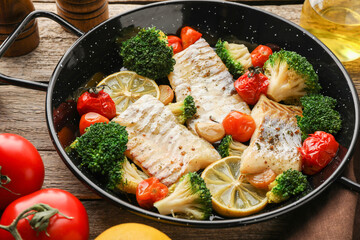 Tasty cod cooked with vegetables in frying pan on wooden table