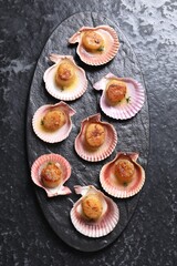 Delicious fried scallops in shells on black table, top view