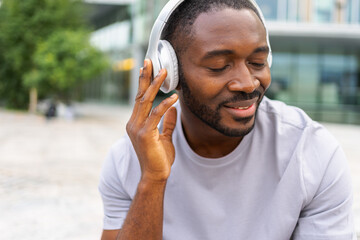 Music song concept. Good start day. Happy African American man listening modern hit on street in...
