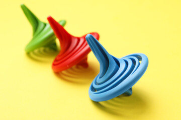 Many colorful spinning tops on yellow background, closeup