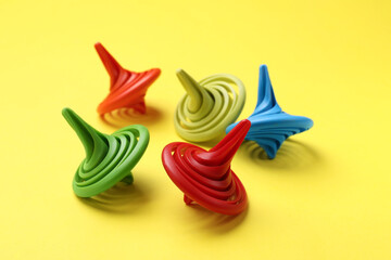 Many colorful spinning tops on yellow background, closeup