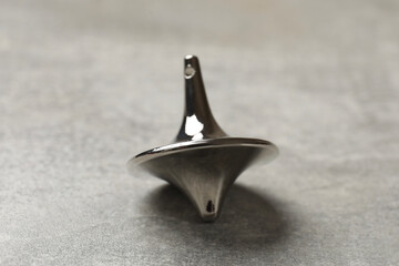 One silver spinning top on grey textured background, closeup