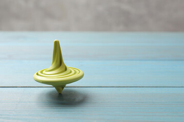 Bright spinning top on light blue wooden table, closeup. Space for text