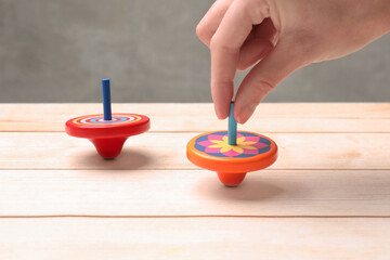 Woman playing with bright spinning top at light wooden table, closeup
