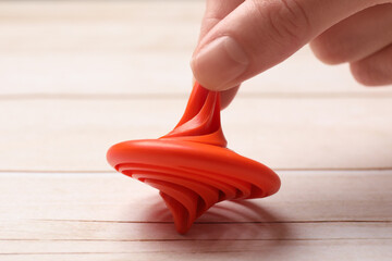 Woman playing with red spinning top at light wooden table, closeup