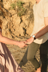 Close up of young beautiful couple holding hands while on a walk at the beach with sandy cliffside background, couple on vacation concept