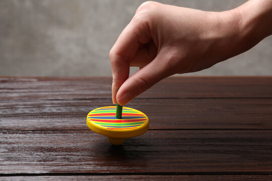 Woman playing with bright spinning top at wooden table, closeup