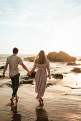 Backview portrait of beautiful young couple in love walking on the beach in California at sunset together, happy couple on vacation concept