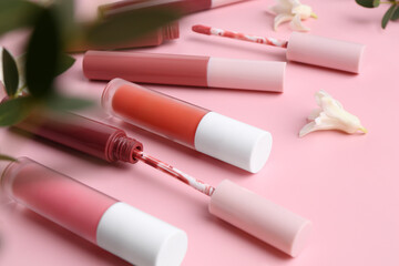 Different lip glosses, applicators, flowers and green leaves on pink background, closeup