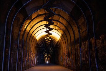 Mysterious graffiti-filled tunnel with a spiraling walkway, illuminated by warm yellow light.