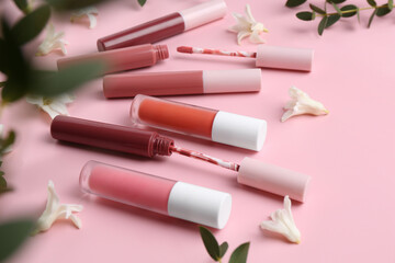 Different lip glosses, applicators, flowers and green leaves on pink background