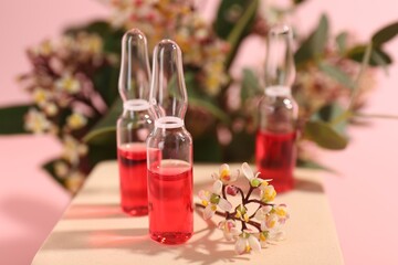 Stylish presentation of skincare ampoules and flowers on pink background, closeup