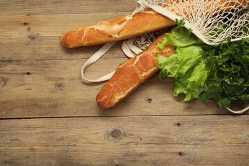 String bag with fresh baguettes, lettuce and herbs on wooden background, top view. Space for text