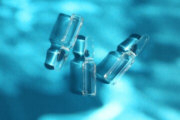 Skincare ampoules in sunlight on light blue background, top view