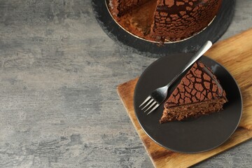 Piece of delicious chocolate truffle cake and fork on grey textured table, above view. Space for...