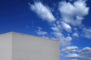 Top of a white windowless building and blue sky with clouds