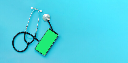 Stethoscope on a blue background and a smartphone with a green screen, top view. Cardiology and...
