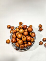 Round jujube in bowl some jujube are on white surface. 