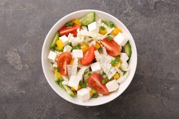 Tasty salad with Chinese cabbage, tomato, cheese, pepper and cucumber on grey table, top view