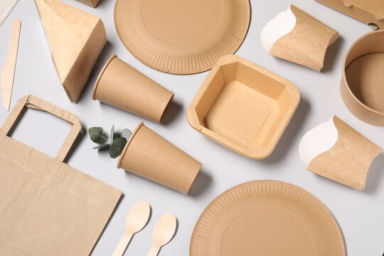 Eco friendly food packaging. Paper containers, tableware and eucalyptus leaves on light grey background, above view
