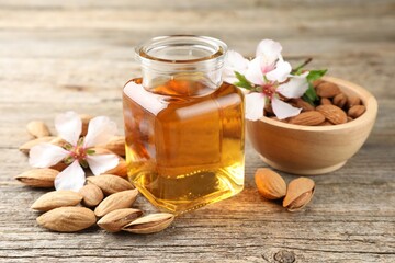 Almond oil in bottle, flowers, bowl and nuts on wooden table, closeup
