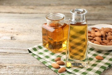 Almond oil in bottles and nuts on wooden table, closeup. Space for text
