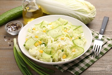 Tasty salad with Chinese cabbage in bowl and ingredients on wooden table, closeup