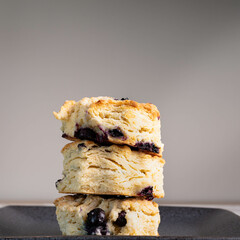 Three stack of fresh blueberry biscuits or scones on a black plate.