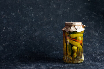 A jar with small cucumbers on a black shabby background. Daylight, selective focus with copy space