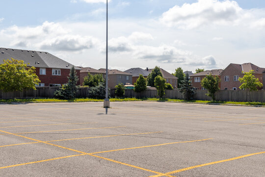 Empty parking lot with lined spaces - lone light pole - suburban homes background - clear sky with clouds. Taken in Toronto, Canada.