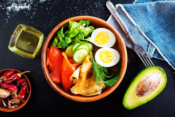 Delicious healthy brunch - boiled egg, smoked salmon, green salad and savory pancakes on a dark background, top view