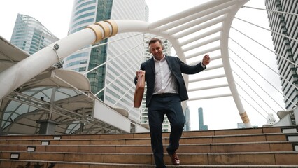 Happy businessman walking down stair and moving to music from headphone. Low angle camera view of...