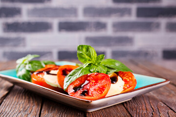 Italian caprese salad with sliced tomatoes, mozzarella, basil, olive oil on wooden background. Top view. - 786632493