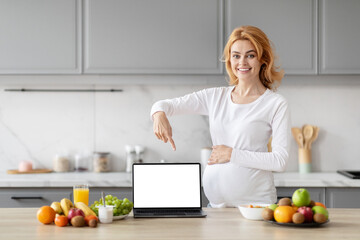 Obraz na płótnie Canvas Pregnant woman using laptop in kitchen, showing nice website