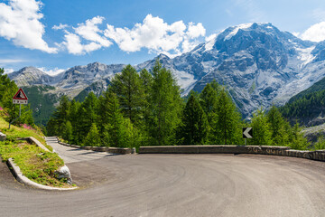 Sharp bend in Stelvio Pass in stunning sunlit Dolomites. Picturesque view of the snow capped mountain range above the winding asphalt road high in the Italian mountains. - Powered by Adobe