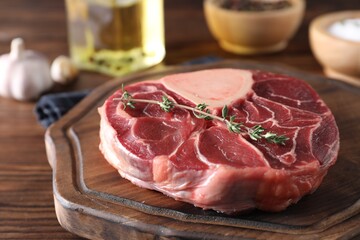 Piece of raw beef meat and thyme on wooden table, closeup