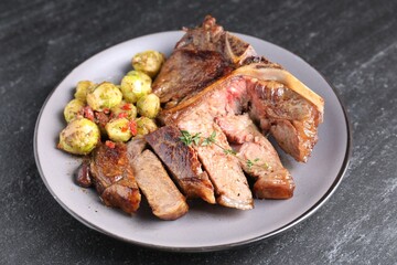 Delicious fried beef meat, vegetables and thyme on black table, closeup