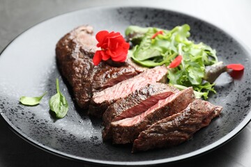 Pieces of delicious grilled beef meat and greens on table, closeup