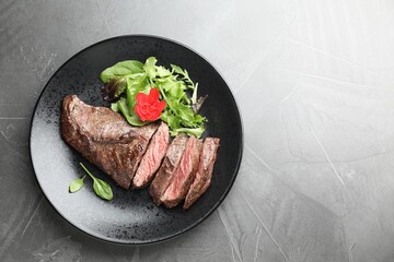 Pieces of delicious grilled beef meat and greens on grey table, top view. Space for text