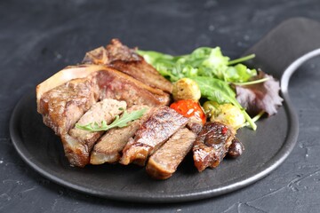 Delicious grilled beef meat, vegetables and greens on black table, closeup