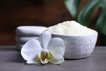 Fototapeta na wymiar Natural sea salt in bowl, spa stones and beautiful orchid flower on wooden table, closeup