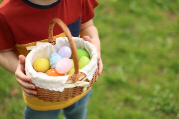 Fototapeta na wymiar Easter celebration. Little boy holding basket with painted eggs outdoors, closeup. Space for text