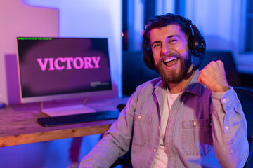 Gamer exuberantly fist pumps with 'VICTORY' on desktop screen